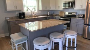 Una cocina moderna con armarios blancos, una isla central con taburetes, electrodomésticos de acero inoxidable e iluminación colgante.