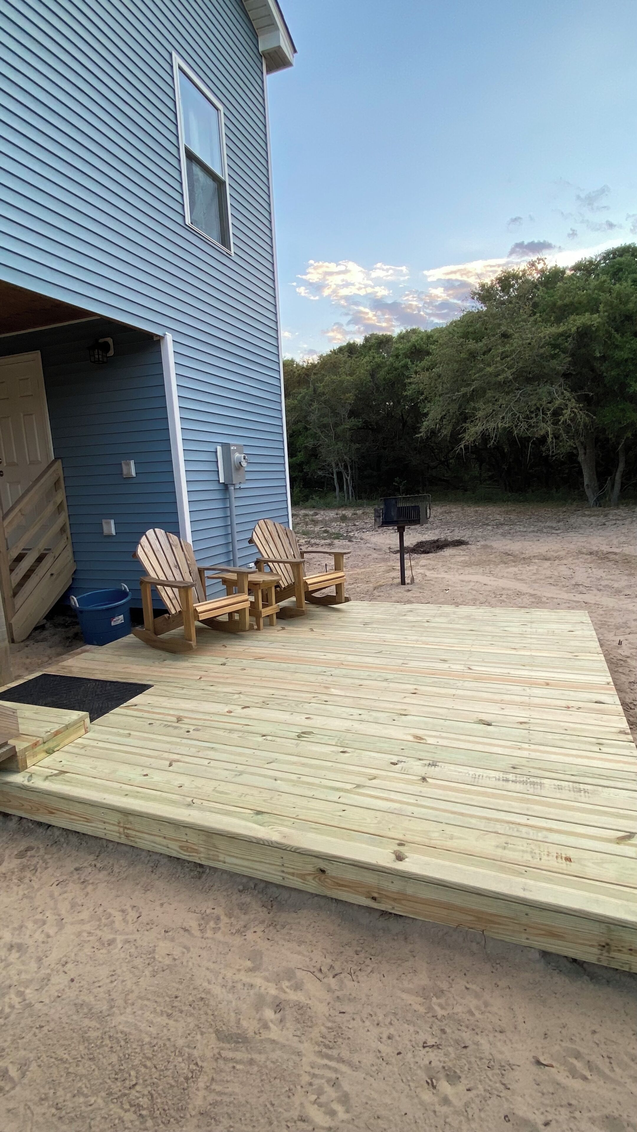 A deck with wooden chairs, a mailbox, and a blue building with a window.