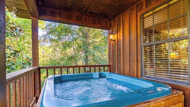A wooden deck with a hot tub, surrounded by trees and a window with blinds. - Wears Valley 3BR Retreat - Hot Tub, Multicade, Pool Table & Hoops! (Sevierville)