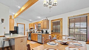 A modern kitchen with wooden cabinets, a central island, and a dining area with a wooden table set for six. - Wears Valley 3BR Retreat - Hot Tub, Multicade, Pool Table & Hoops! (Sevierville)
