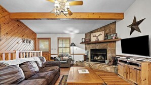 A cozy living room with a fireplace, leather sofa, wooden coffee table, and a TV. - Wears Valley 3BR Retreat - Hot Tub, Multicade, Pool Table & Hoops! (Sevierville)