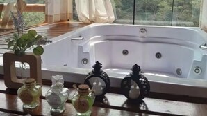 A wooden deck with a hot tub, surrounded by white curtains and a view of a forested area. - Chalé Recanto da Mata - Romantic chalet with mountain views and a hot tub. (Sapucaí-Mirim)