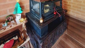 A brick-walled room with a wood-burning stove, a small Christmas tree, and a shelf with various items. - Chalé Recanto da Mata - Romantic chalet with mountain views and a hot tub. (Sapucaí-Mirim)