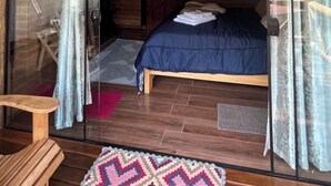 A room with a bed, a wooden table, and a patterned rug. - Chalé Recanto da Mata - Romantic chalet with mountain views and a hot tub. (Sapucaí-Mirim)