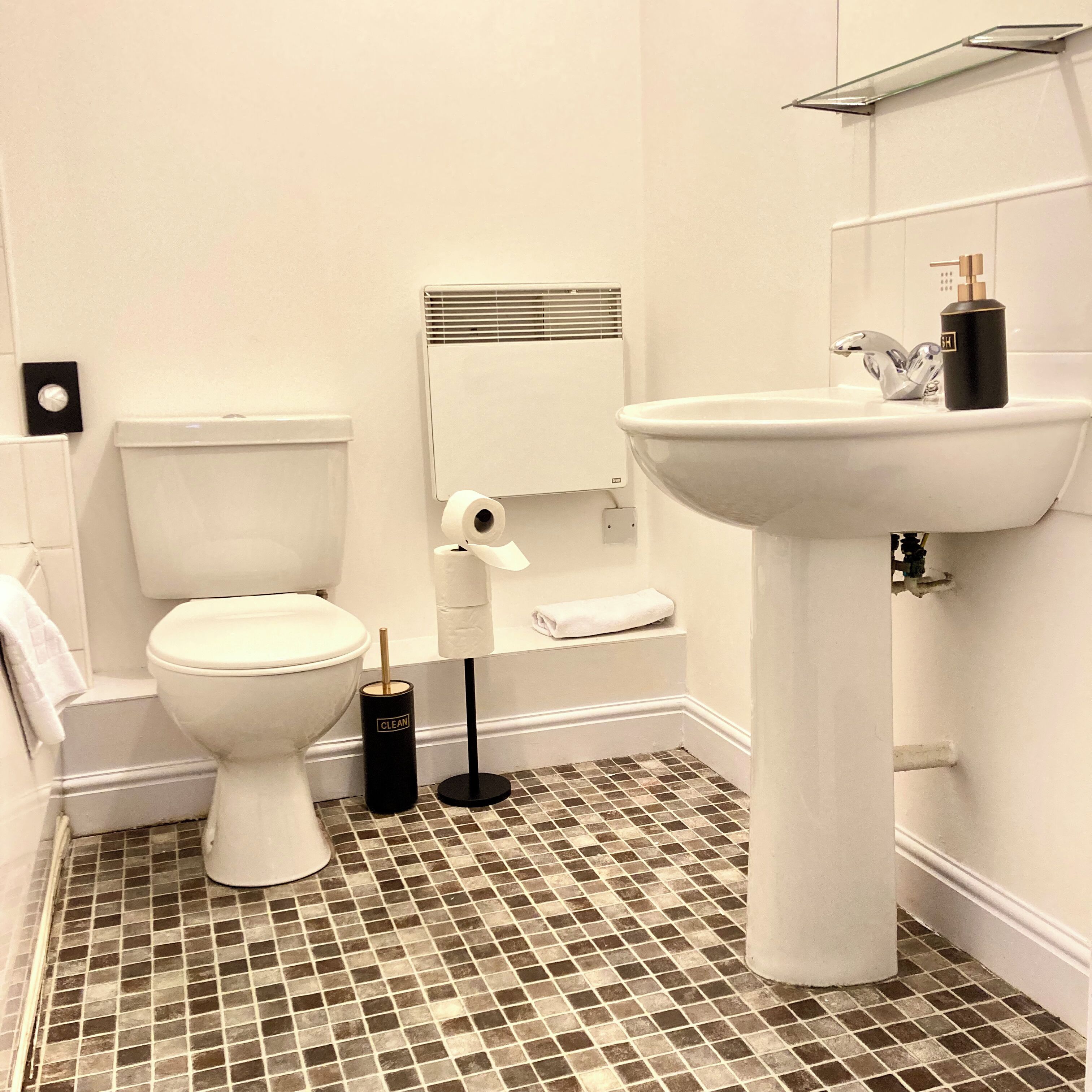 A bathroom with a toilet, a sink, a mirror, and a roll of toilet paper.