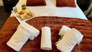Una cama bien hecha con una manta marrón, dos almohadas marrones y un plato de alimentos para el desayuno.