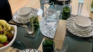 Comedor con una mesa dispuesta para cuatro personas, rodeado de un papel tapiz estampado y un sofá verde.