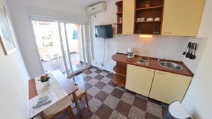 Une cuisine de taille réduite avec un carrelage à motifs, une table à manger avec des chaises, un téléviseur fixé au mur et un évier.