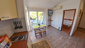 Cocina compacta con comedor, televisor pequeño y dormitorio con cama y mesita de noche.