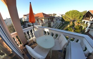 A balcony with a round table and two chairs, a red umbrella, and a view of a residential area with houses and trees. - 1 bedroom stunning apartment in Turanj (Turanj)