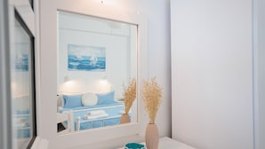 Une salle de bain avec un meuble-lavabo blanc, un miroir, un bol bleu et deux vases contenant des fleurs séchées.