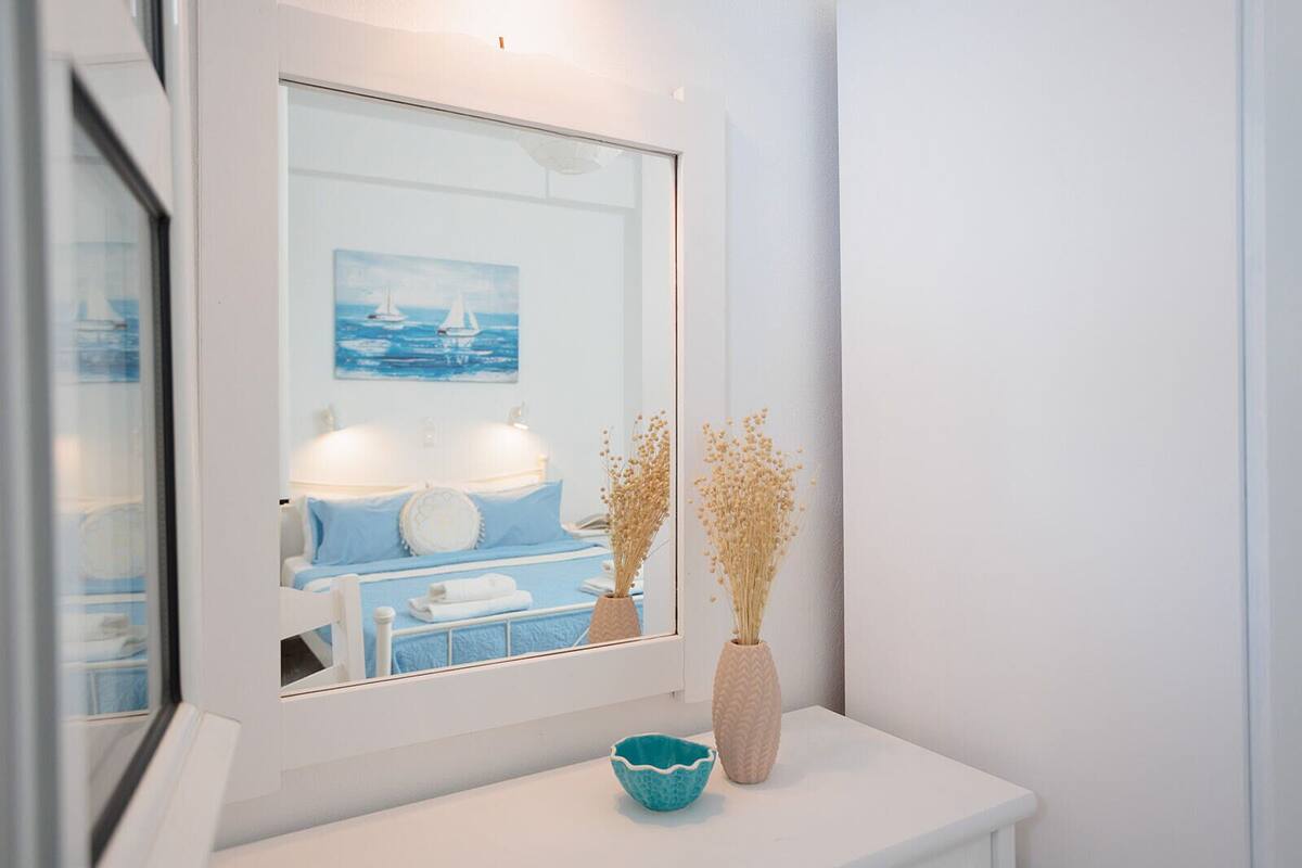 A bathroom with a white vanity, a mirror, a blue bowl, and two vases with dried flowers.