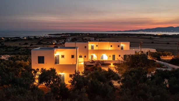 Un bâtiment moderne doté de nombreuses pièces, entouré d’une végétation luxuriante et offrant une vue sur le littoral au coucher du soleil.
