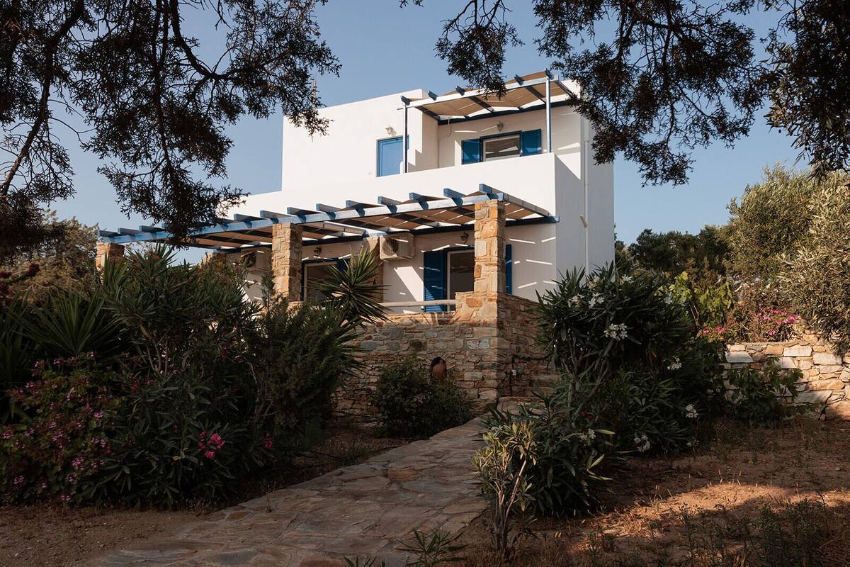 A modern two-story house with a stone foundation, a covered porch with blue railings, and a garden with various plants and flowers.
