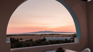 Un balcon donnant sur un paysage au coucher du soleil, une table avec une assiette et une chaise.
