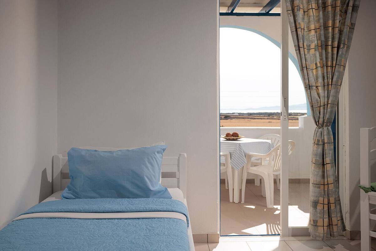 A bedroom with a bed, a view of the balcony, and a dining area with a table and chairs.