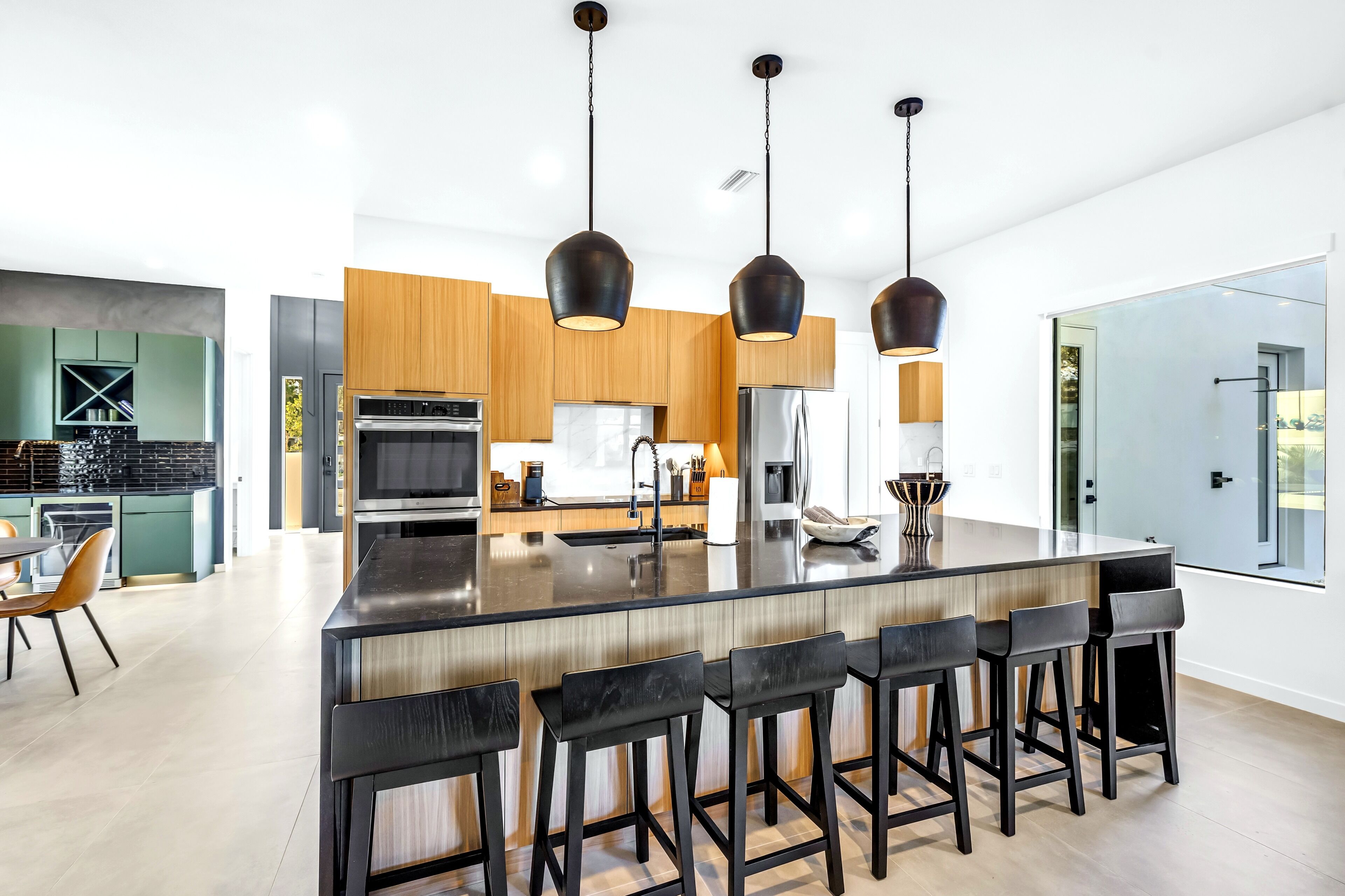 Une cuisine moderne dotée d’un îlot central, de tabourets de bar et de luminaires suspendus.