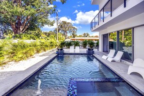 A modern pool with clear water, surrounded by lush greenery and a contemporary building with large windows. - Temple of Time- Stunning new modern home w/pool (Sarasota)