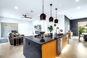 A modern kitchen with a central island, pendant lighting, and a dining area with a table and chairs. - Temple of Time- Stunning new modern home w/pool (Sarasota)