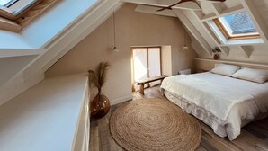 Slaapkamer met dakraam, plafondventilator, een bed, nachtkastje, vaas en een geweven vloerkleed.