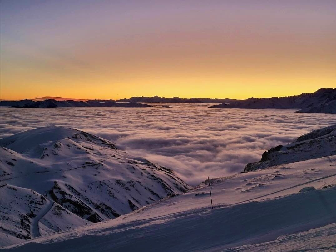 Paisagem montanhosa coberta de neve com céu claro ao pôr do sol.