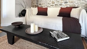 Een gezellige kamer met een stenen muur, een houten plafond, een witte bank, een zwarte tafel en een lamp.