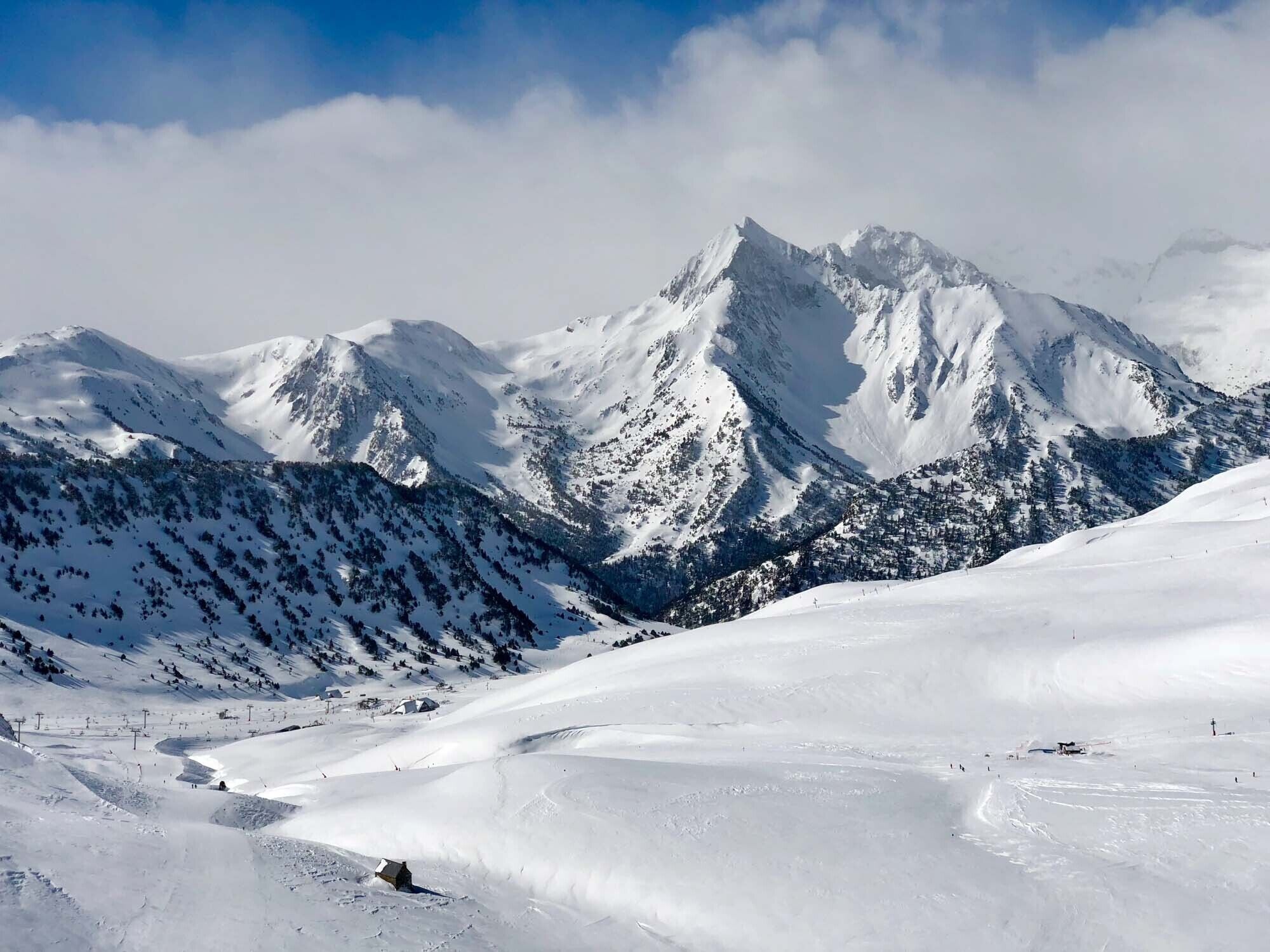 Een besneeuwd berglandschap met skipistes en een klein berghuis.