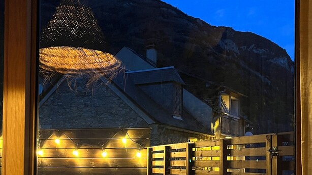 Een houten terras met een bank en tafel, sfeerverlichting en uitzicht op een berg in de schemering.