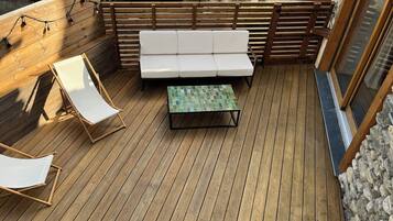 Eine Holzterrasse mit einem weißen Sofa, zwei weißen Liegestühlen und einem grünen Tisch mit Muster.