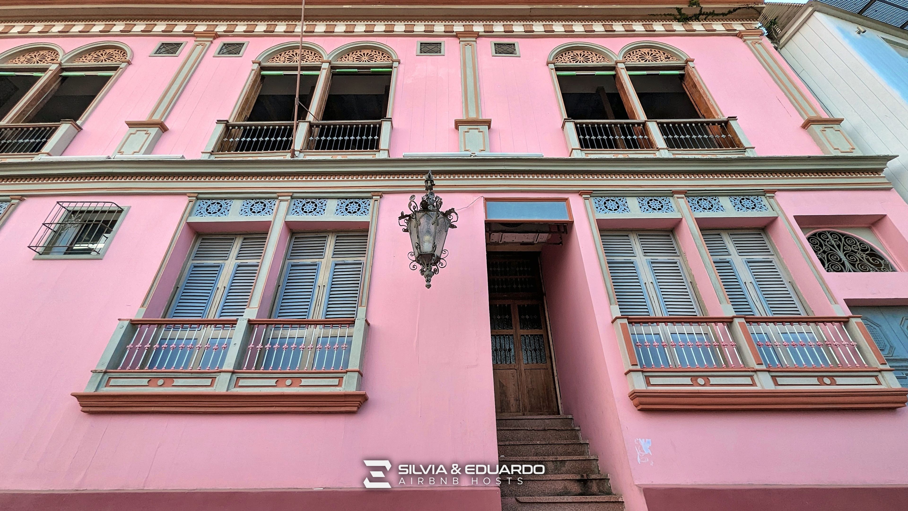 Un bâtiment rose doté de nombreuses fenêtres, de balcons et d’un escalier menant à l’entrée.