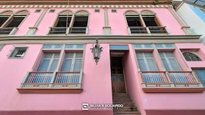 A pink building with multiple windows, balconies, and a staircase leading to the entrance. - Puerto Santa Ana · 2 Suites · Pool, Jacuzzi & Gym · Self Check-in (Guayaquil)