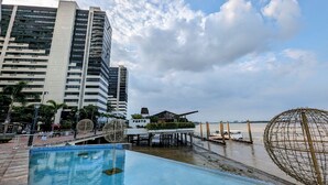 Ein Hotel am Wasserufer mit Pool, Strandbereich und hohen Gebäuden im Hintergrund.