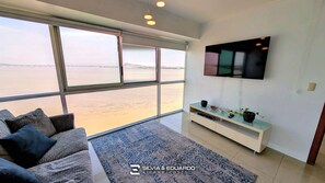 A modern living room with a large window, a flat-screen TV, and a sofa. - Puerto Santa Ana · 2 Suites · Pool, Jacuzzi & Gym · Self Check-in (Guayaquil)