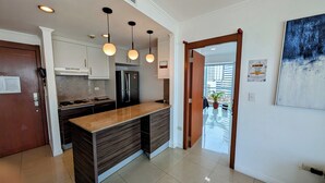 Eine moderne Küche mit Granit-Arbeitsplatten, einem eingebauten Backofen und einem Edelstahl-Kühlschrank. Über der Kochinsel hängen Pendelleuchten und durch eine Glastür ist der Außenbereich sichtbar.