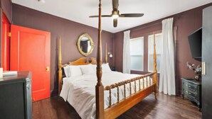 Ein Schlafzimmer mit Himmelbett, Deckenventilator, großem Spiegel und roter Tür.