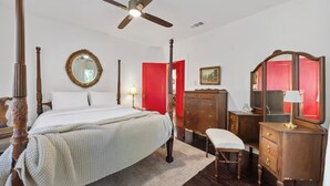 Ein Bett mit Baldachin, ein Deckenventilator, eine Holzkommode, eine Bank und eine rote Tür.