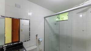 Une salle de bain avec des carreaux blancs, une douche en verre, des toilettes, un lavabo avec un plan de travail noir et un miroir avec un cadre en bois.