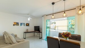 Un salon comprenant un canapé, un téléviseur, une table à manger avec des chaises et un balcon avec vue.