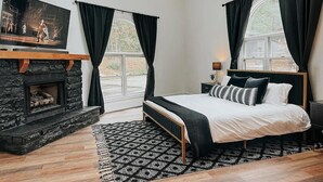 Um quarto com lareira de pedra, cama com tapete de padrão preto e branco, e uma janela grande com cortinas.