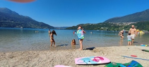A lake with people swimming and standing in shallow water, surrounded by mountains.