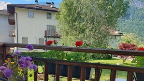 A balcony with a round table, a vase with flowers, and a view of a mountain and a car in the background. - Farmhouse in typical Trentino style, spacious, elegant, comfortable. (Civezzano)