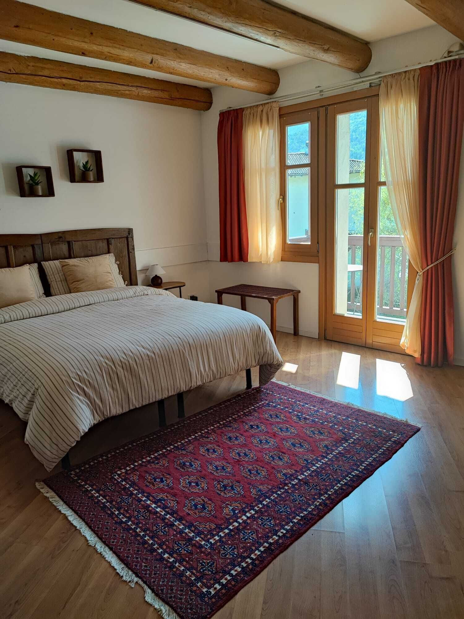 Una camera da letto con un letto grande, una testiera in legno, un tavolino e un'ampia finestra con tende.