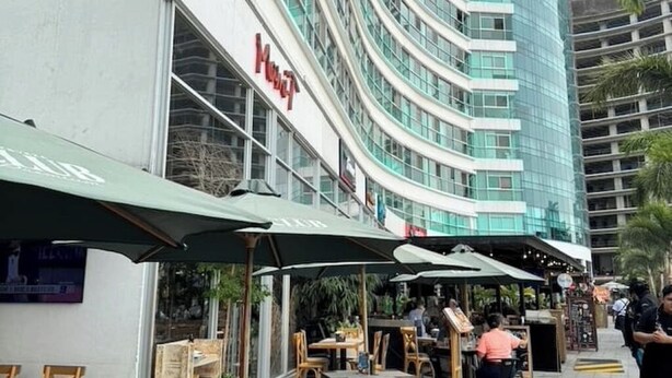 Un hotel amb façana corbada, zona d'estar exterior amb ombrel·les i un rètol de restaurant visible.