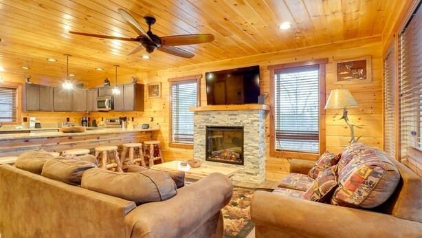 Acogedor interior de cabaña de madera con chimenea, muebles de madera y una zona de cocina.