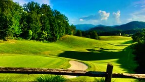Un campo de golf con valla de madera, césped verde exuberante y árboles al fondo.