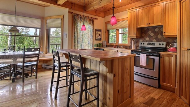 A kitchen with wooden cabinets, a large island with bar stools, a stainless steel stove, and hanging pendant lights.