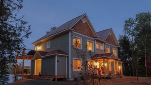 A two-story house with a porch, a garage, and a deck overlooking a body of water.