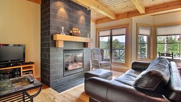 Ein Wohnzimmer mit Kamin, einer Ledersofa, einem Fernseher und einer Holzbalkendecke.