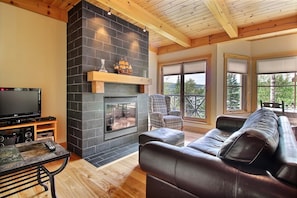 Una sala de estar con chimenea, un sofá de cuero, un televisor y techo de madera.