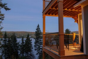 A wooden deck with a railing overlooking a lake, surrounded by trees.